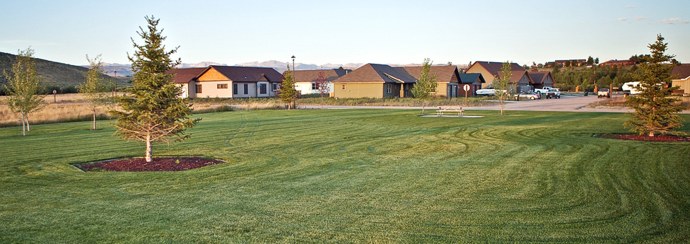 One-acre community park at Split Diamond Meadows with manicured lawn, young trees, and homes in the background